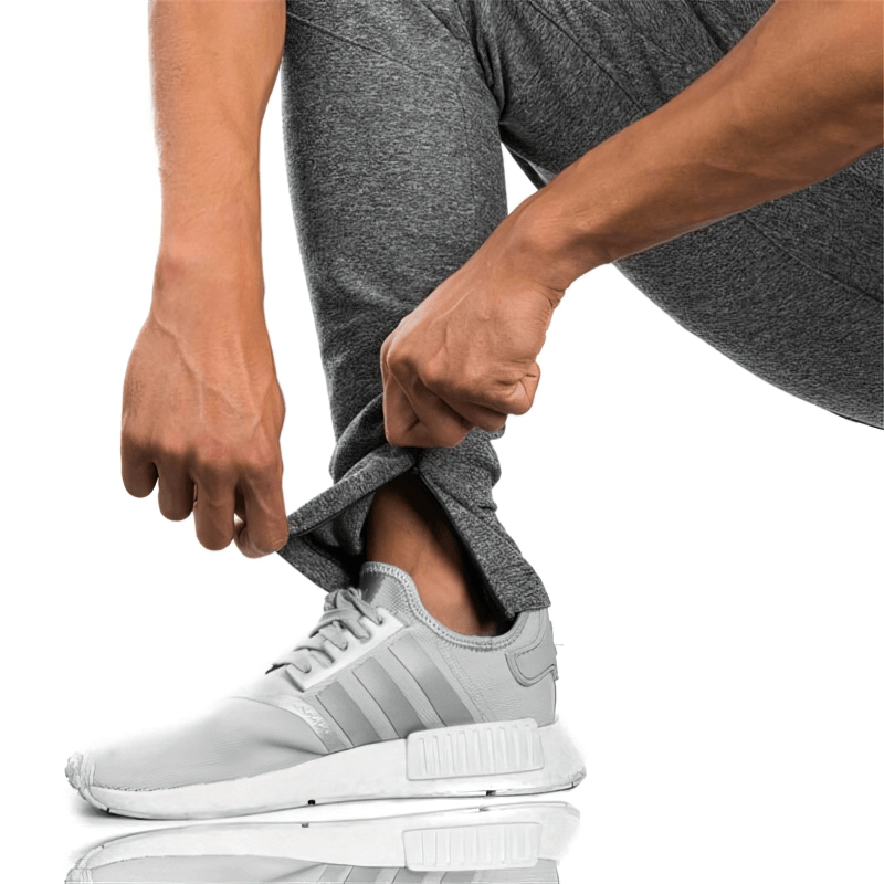 Man wearing sports elastic quick-drying pants, adjusting leg cuff over white sneakers, illustrating comfort and flexibility.