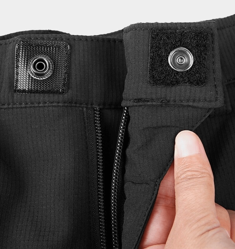Close-up of the secure button and zipper closure on black sports windproof women's hiking pants with elastic waistband.