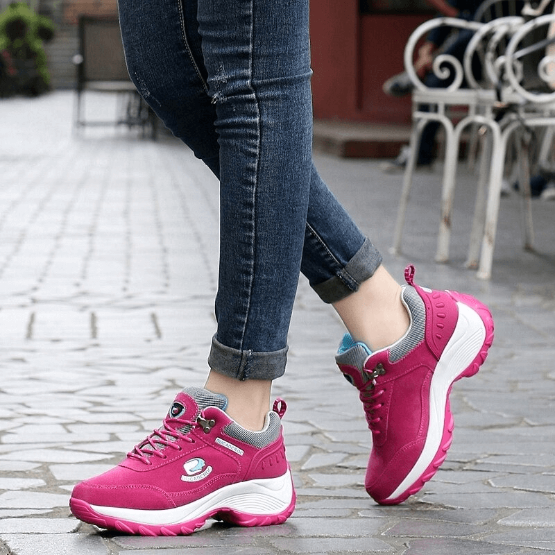 Woman wearing pink sports fur sneakers with jeans, showcasing stylish and insulated footwear on a cobblestone street.