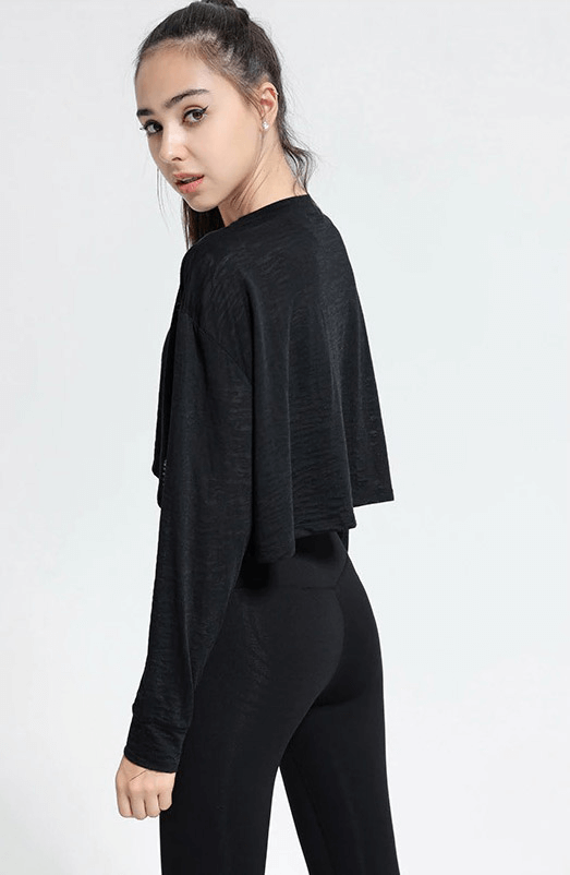 Woman wearing black sports long-sleeved loose top, ideal for fitness, yoga, gym, made of breathable cotton and polyester.