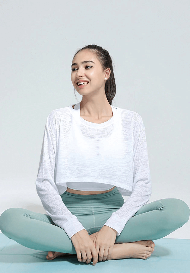 Woman wearing an oversized white long-sleeve top sitting cross-legged on a mat, ideal for yoga and fitness activities.