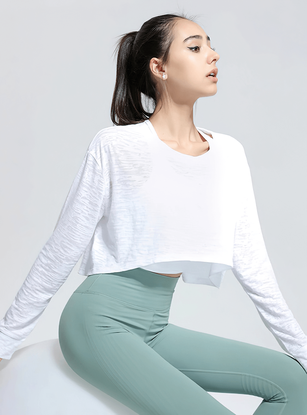 Woman wearing a white sports long-sleeved loose top and green leggings, perfect for yoga, pilates, gym, and fitness activities.