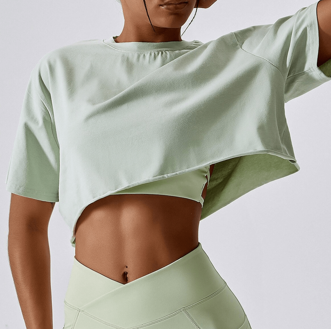 Woman wearing a sports loose crop top, light green, O-neck, perfect for running and yoga, made from breathable fabric. Model shows stylish design.