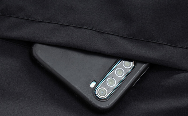 Smartphone slipping into pocket of sports men's jacket, showcasing spacious and secure design.