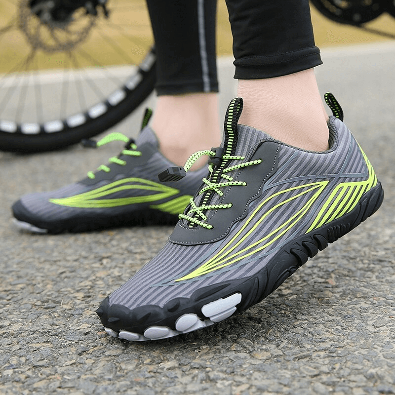 Person wearing lightweight sports mountain bicycle sneakers with green accents on asphalt near bike wheel.