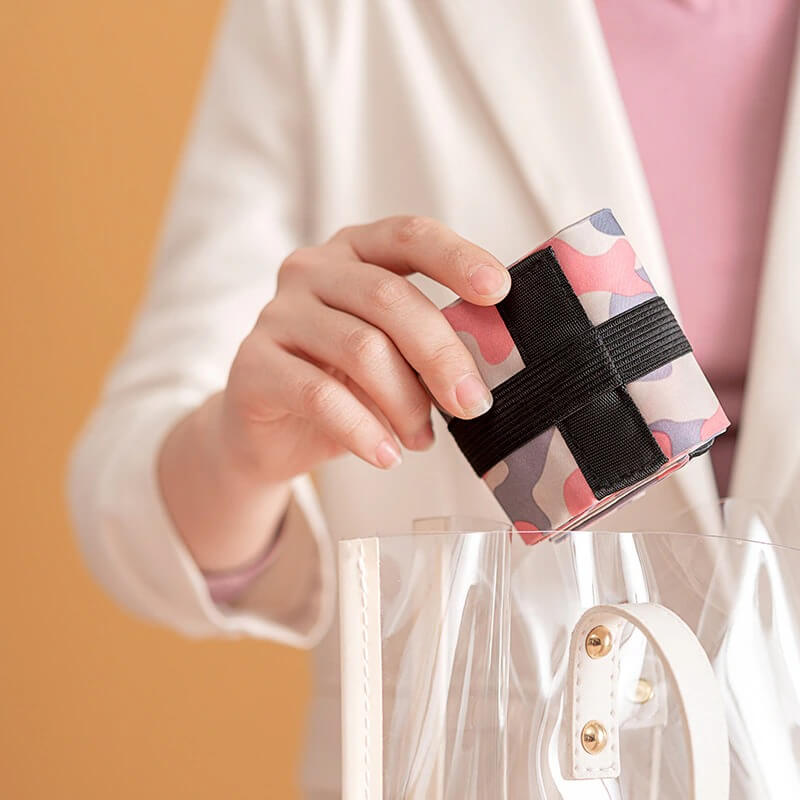 A woman placing a folded pink and black patterned fabric into a clear bag, highlighting portability and design.