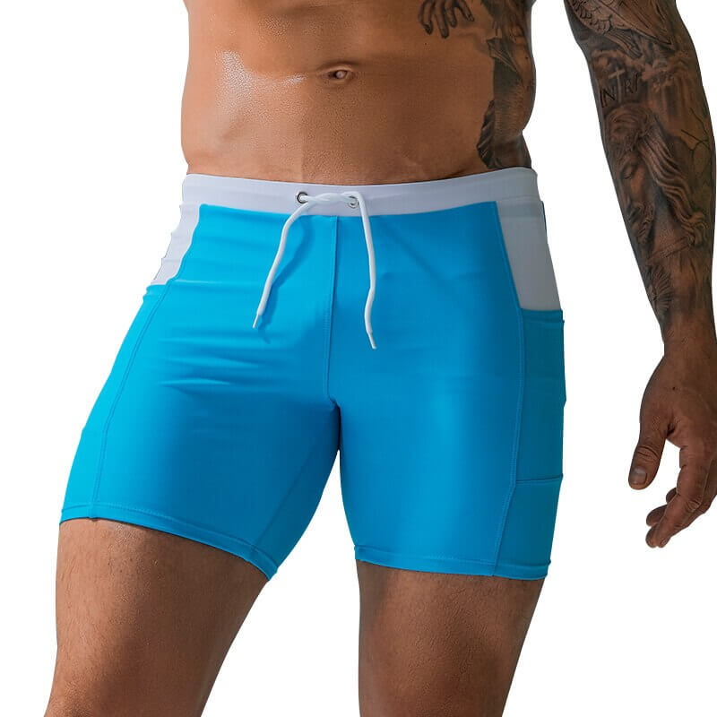 Blue waterproof beach boxer shorts with white drawstring and pockets, worn by a tattooed model, perfect for sports and water activities.