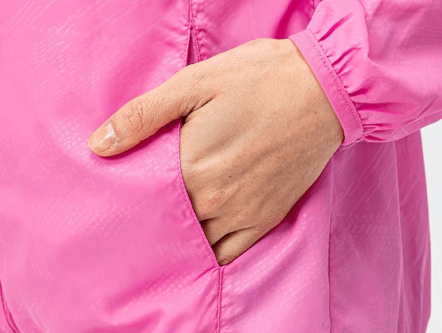 Close-up of a pink waterproof windbreaker jacket pocket with hand inside, showcasing durable polyester material for active women.