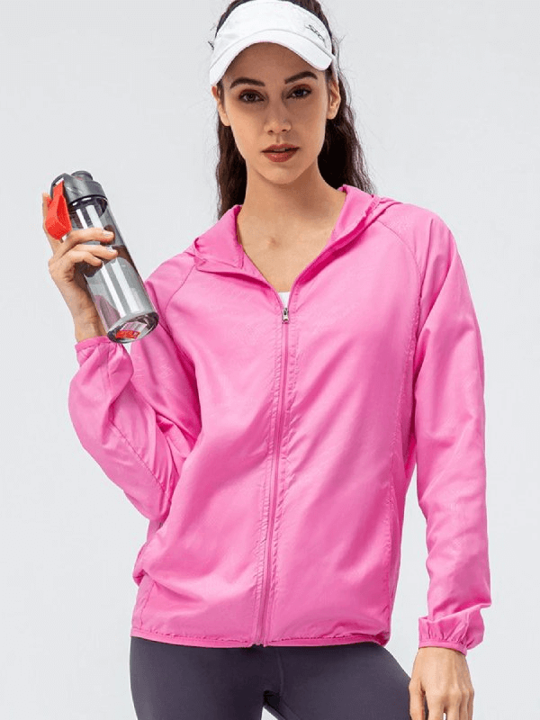 Woman in pink waterproof windbreaker holding a water bottle, ideal for running. Features hood, zipper, and breathable polyester.