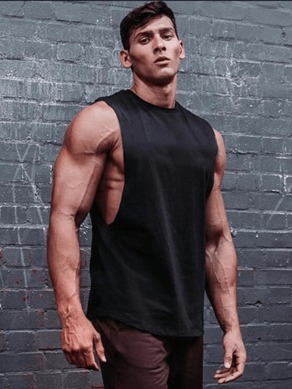 Man wearing a black sporty quick-drying tank with dropped armholes, showing off athletic build against a textured brick wall.