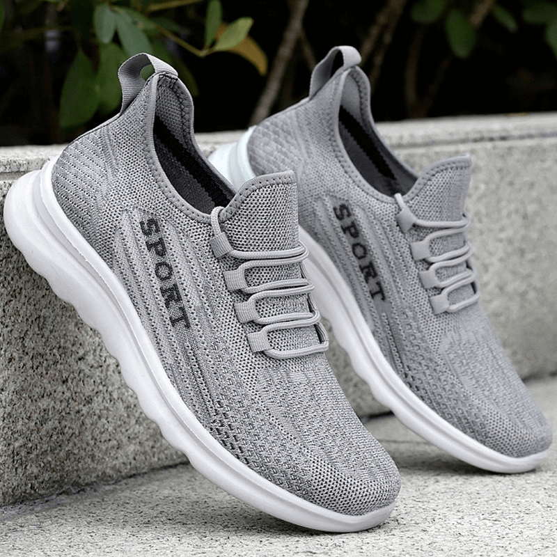 Gray stylish breathable elastic lace up sneakers for men with mesh design and solid pattern, sitting outdoors on stone ledge.