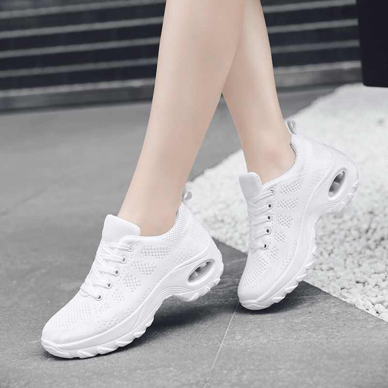 White stylish breathable flexible women's sneakers SF0775 with mesh air upper and non-slip sole on model's feet on pavement.