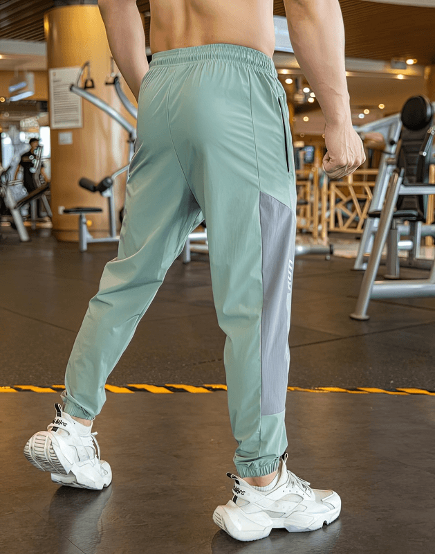 Man wearing stylish quick-drying sporty men's pants with cuffs for training, perfect for running, shown in gym setting with sneakers.