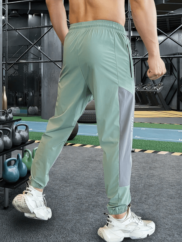 Man wearing sporty quick-drying green pants with cuffs, ideal for running, standing in a gym setting with kettlebells in the background.