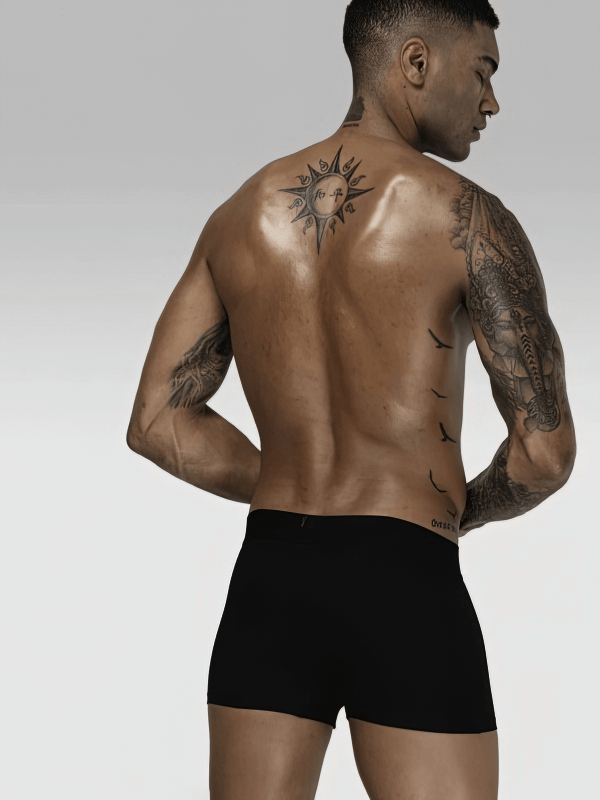 Back view of a man wearing stylish soft black men's boxers, showcasing tattoos on a muscular back against a neutral background.