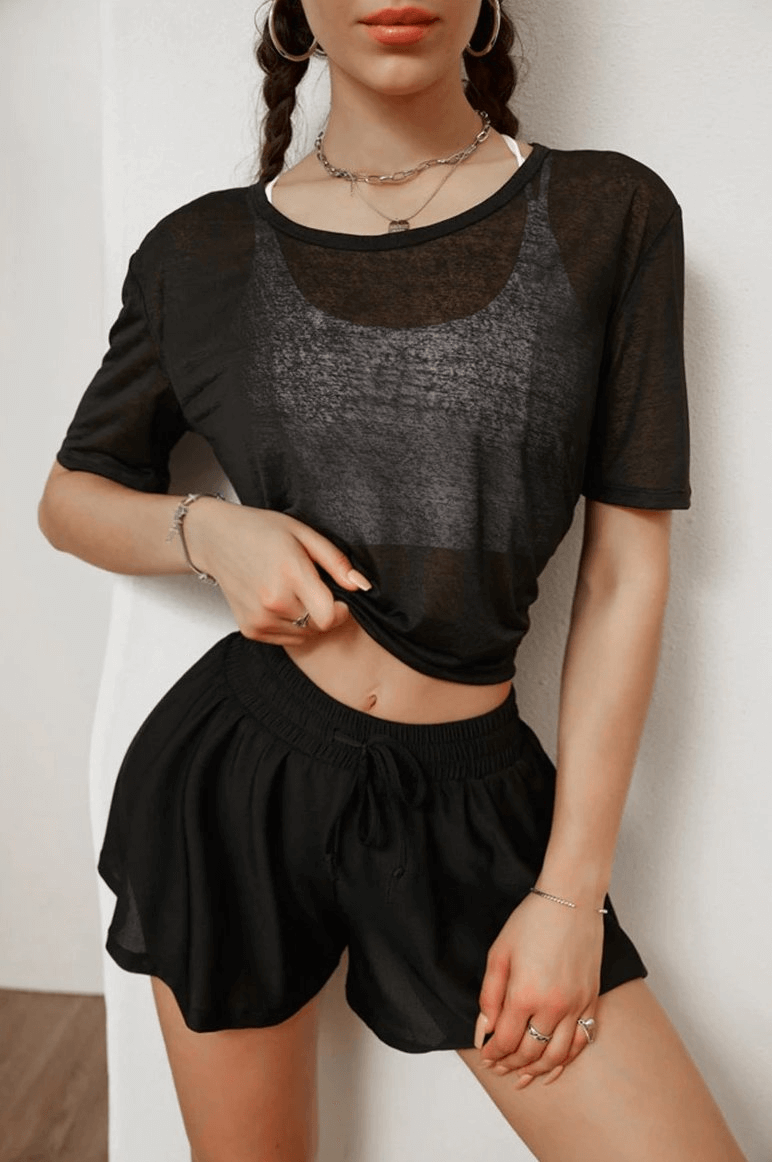Woman wearing a stylish translucent black top with open back and tie-up, perfect for yoga, featuring short sleeves and breathable material.