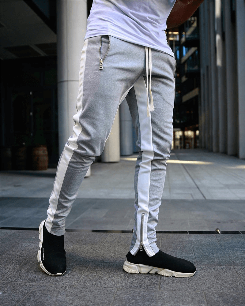 Stylish two-tone men's jogging pants with zipper pockets and drawstring, perfect for comfortable running. Model in urban setting.