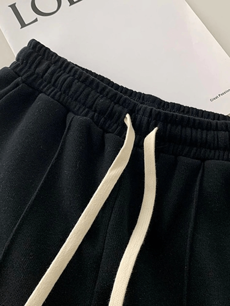 Close-up of stylish high-waist black women's shorts with side pockets and drawstring, on a white fabric backdrop.
