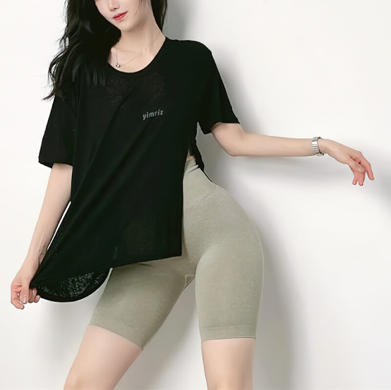 Woman modeling a stylish black top with side cut and beige cycling shorts, designed for yoga and training.