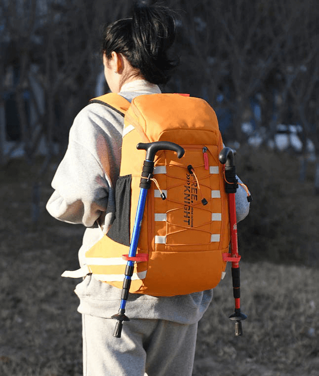 Person wearing an orange travel backpack 40L with hiking poles attached, enjoying outdoor adventure.