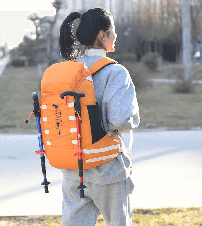 Person wearing orange 40L travel backpack with rain cover on a hike, showing outdoor sports bag features and trekking poles.