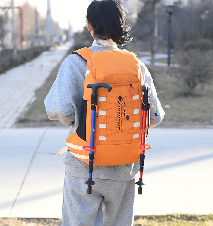 Person wearing orange 40L travel backpack with trekking poles attached, perfect for outdoor sports and hiking adventures.
