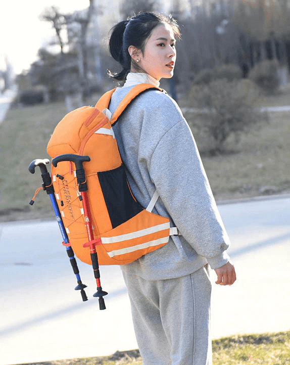 Person wearing a Travel Backpack 40L with Rain Cover for outdoor sports, featuring a vibrant orange color and trekking poles attached.