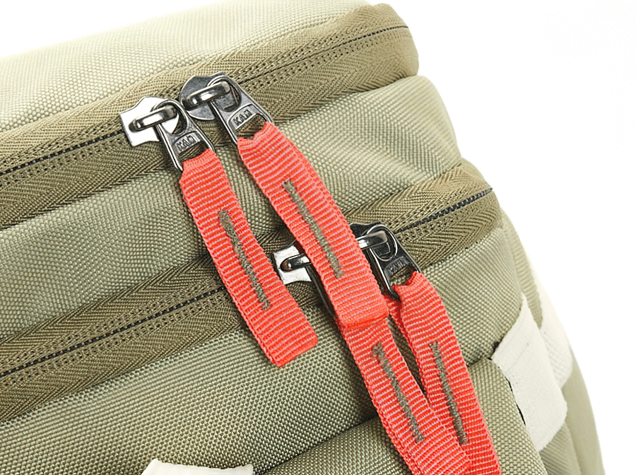 Close-up of travel backpack double zippers with red pull tabs on khaki fabric. Ideal for outdoor activities and adventure trips.