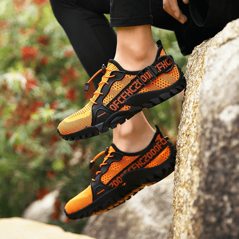 Unisex orange trekking flexible hiking boots on rocky path, breathable design, size 36-47, for adventurous outdoor comfort.