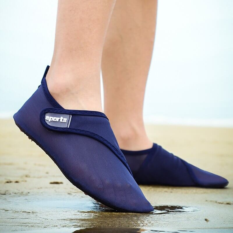 Person wearing unisex navy mesh water shoes at the beach, showcasing breathable and flexible design with rubber outsole.
