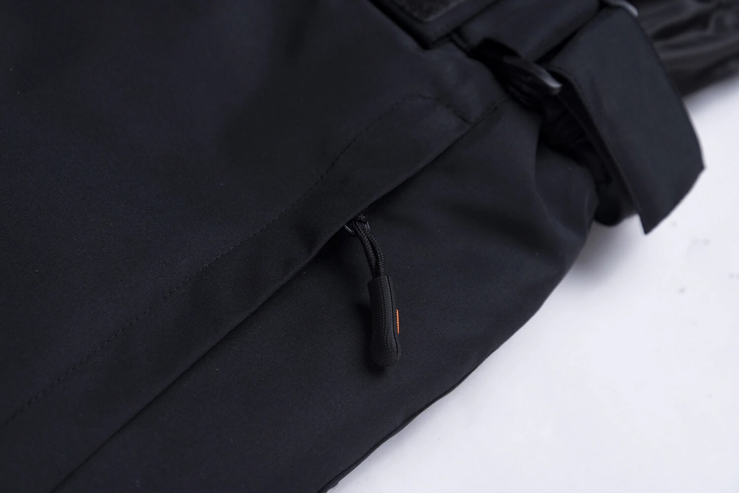 Close-up view of black ski trousers featuring a zipper and suspenders, offering warmth and comfort for unisex skiing adventures.