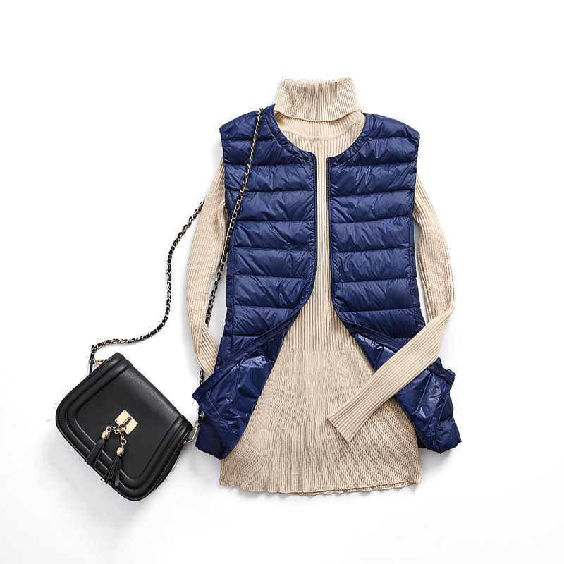 Navy blue women's ultra-light vest with pockets on beige sweater, paired with a stylish black handbag.