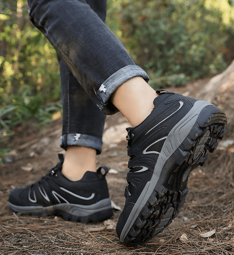 Man wearing waterproof anti-slip trekking shoes, black design with rubber sole, walking outdoors. Ideal for hiking adventures.