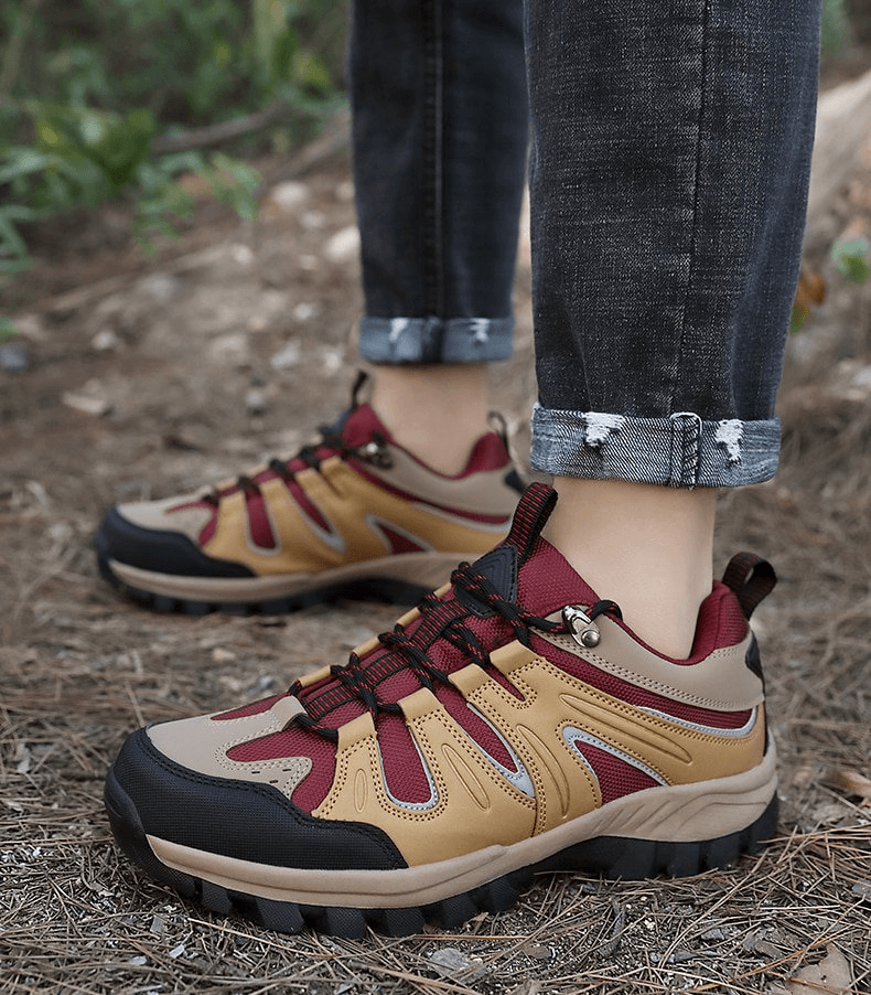 Brown and red waterproof anti-slip men's trekking shoes on forest floor, showcasing durable rubber outsoles and secure lace-up design.