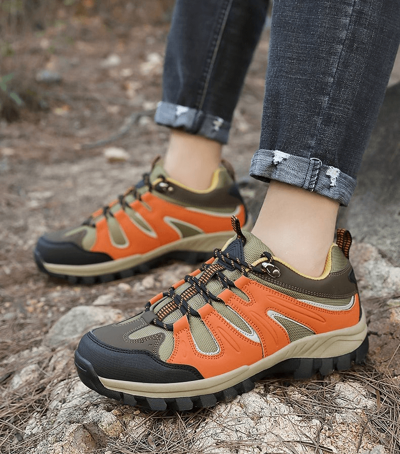 Orange waterproof anti-slip men's trekking shoes with rubber outsole and lace-up closure on rocky outdoor terrain.