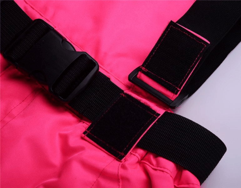 Close-up of pink waterproof breathable insulated ski pants with black suspenders and velcro straps for secure fitting.