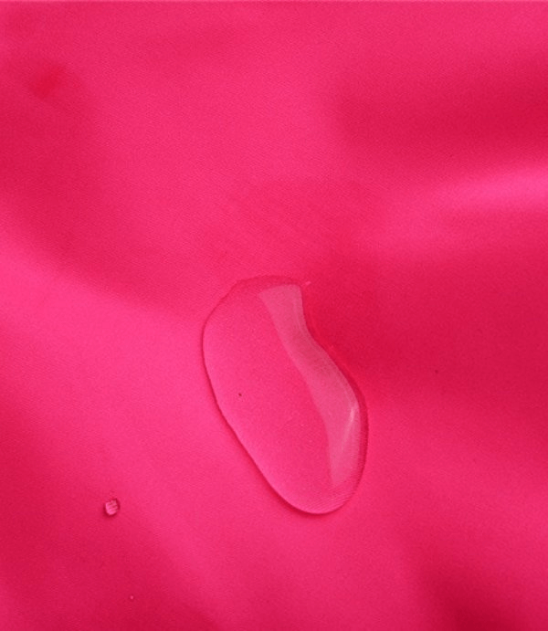 Close-up of waterproof fabric with water droplet on pink nylon-polyester ski pants.