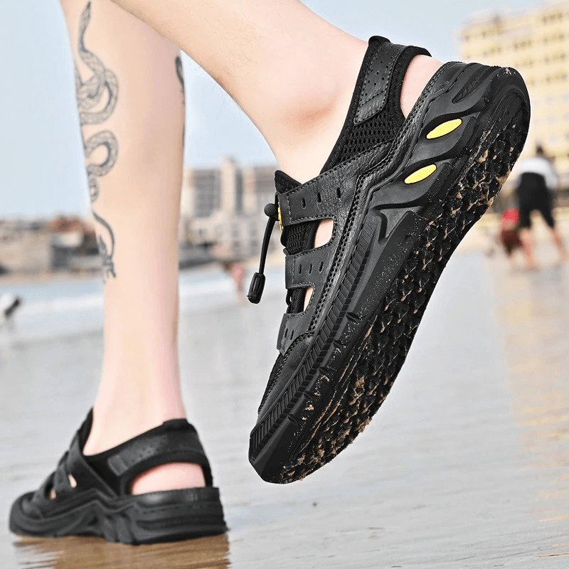 Person wearing black hollow-out breathable mesh sandals on beach.