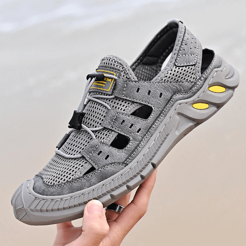 Gray breathable mesh sandal with wear-resistant PVC sole, featuring hollow-out design and elastic band closure held in a hand.