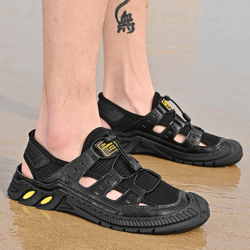 Hollow-out breathable mesh sandals with wear-resistant rubber sole worn on sandy beach. Perfect blend of style and comfort.