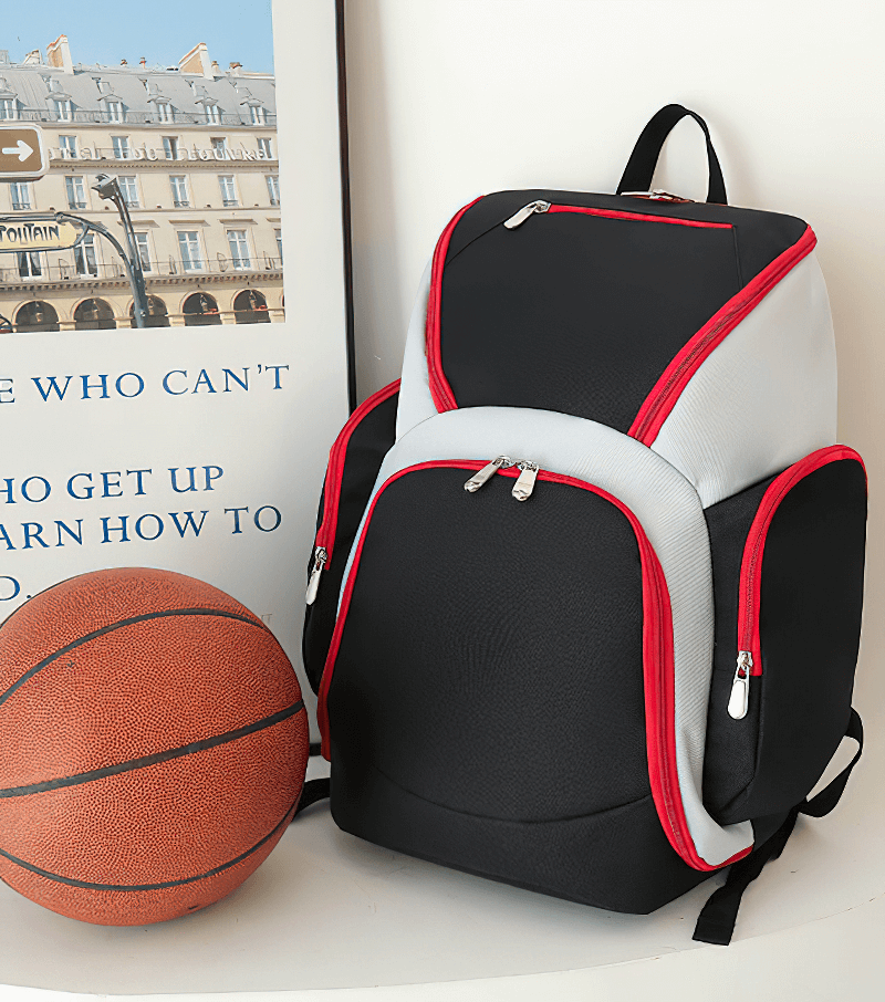 Waterproof lightweight football backpack with red accents and large capacity next to a basketball for sports convenience.