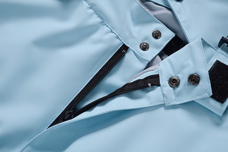 Close-up of blue waterproof snowboarding trousers with zipper fly and buttons, featuring waist protection for extreme weather conditions.