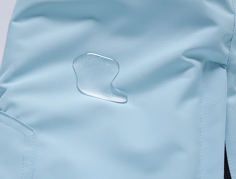 Close-up of blue waterproof snowboarding trousers repelling water droplet, showcasing fabric texture and weather resistance.