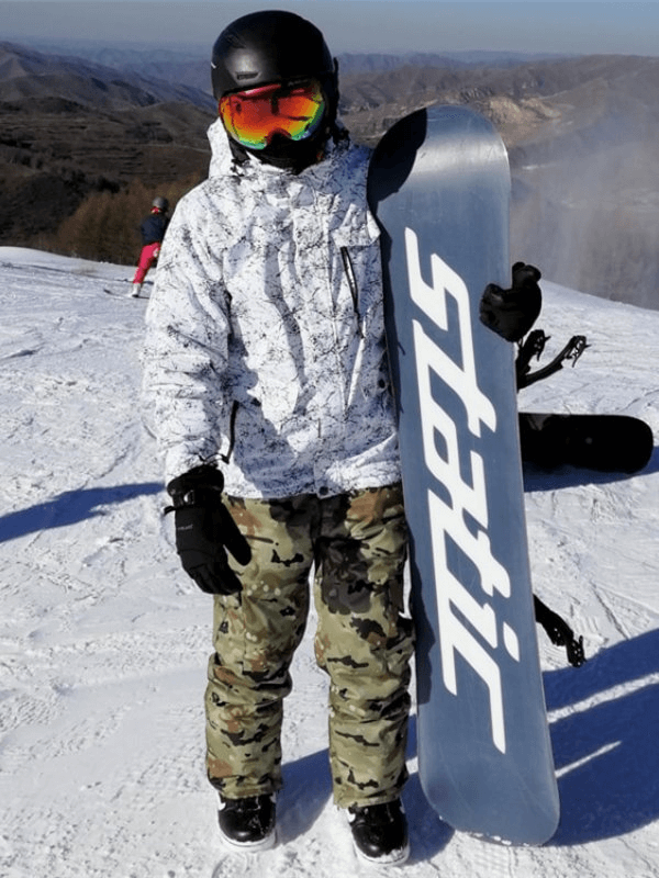 Snowboarder in camo pants and white jacket holding snowboard on snowy mountain