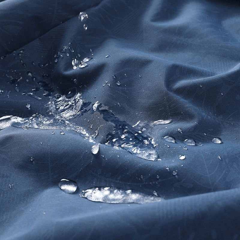 Water droplets on blue waterproof fabric demonstrating the material of men's quick dry raincoats with windproof technology.