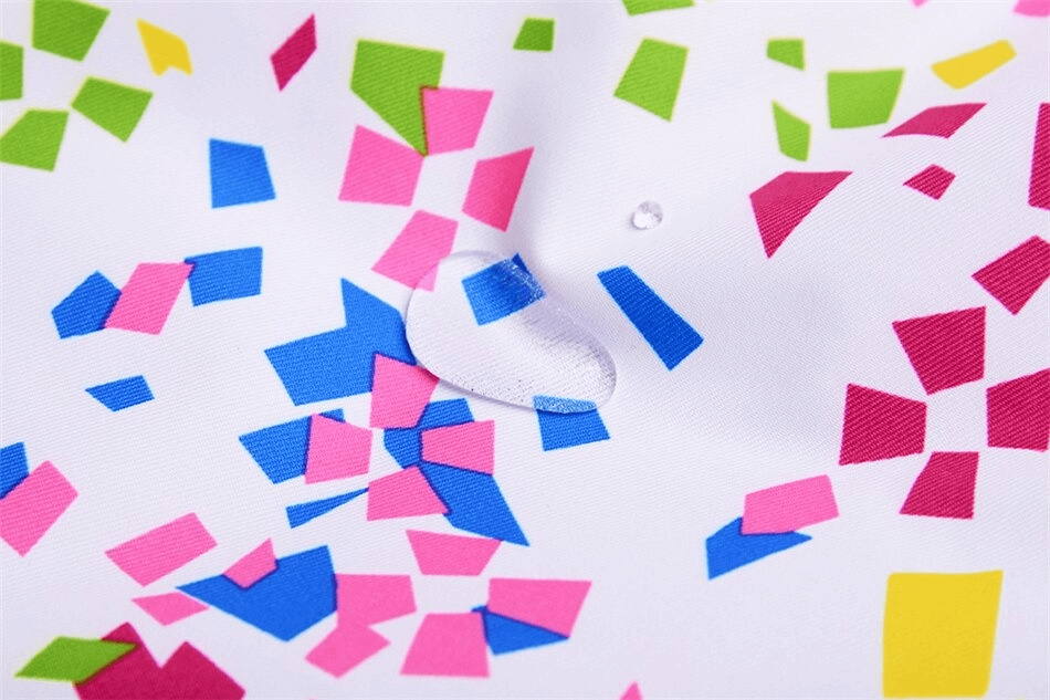 Close-up of colorful, geometric confetti design on fabric, demonstrating water resistance with a droplet on the surface.