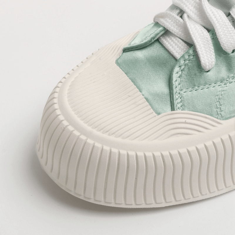 Close-up of women's casual lace-up sports shoe with thick flat sole and mint green silk upper.
