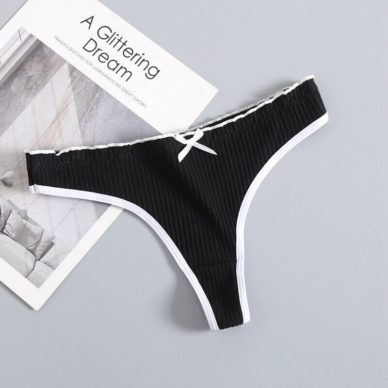 Women's black cotton low-rise T-back G-string with bow, laid on a magazine, showcases stylish and breathable lingerie design - SF0967.