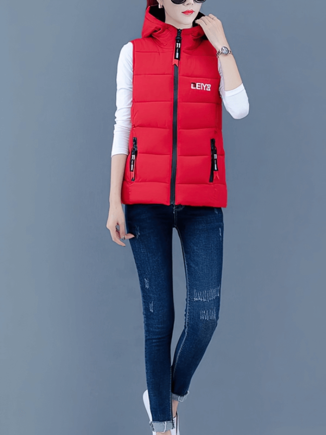 Red women's down vest with hood and zippered pockets worn by model, paired with dark jeans and white sneakers.