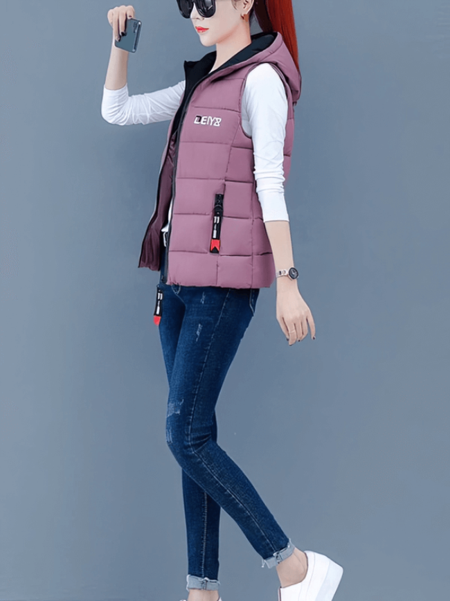 Woman in pink down vest with zipper pockets, wearing jeans and white sneakers, holding a phone, styled for cool weather.